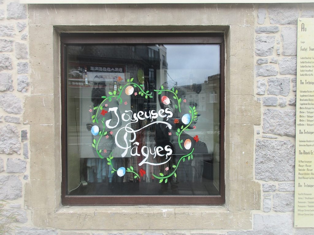 Joyeuses Pâques écrit en blanc à la main sur une vitrine avec des œufs colorés et des branches fleuries