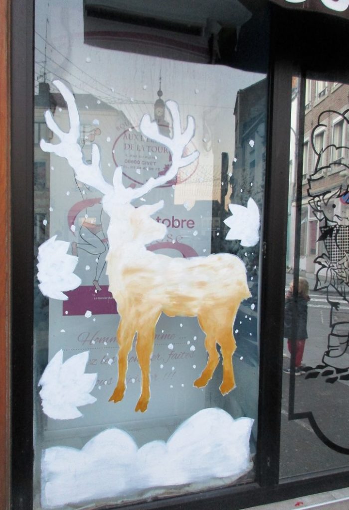 cerf blanc et or peint sur une vitrine avec de la neige qui tombe