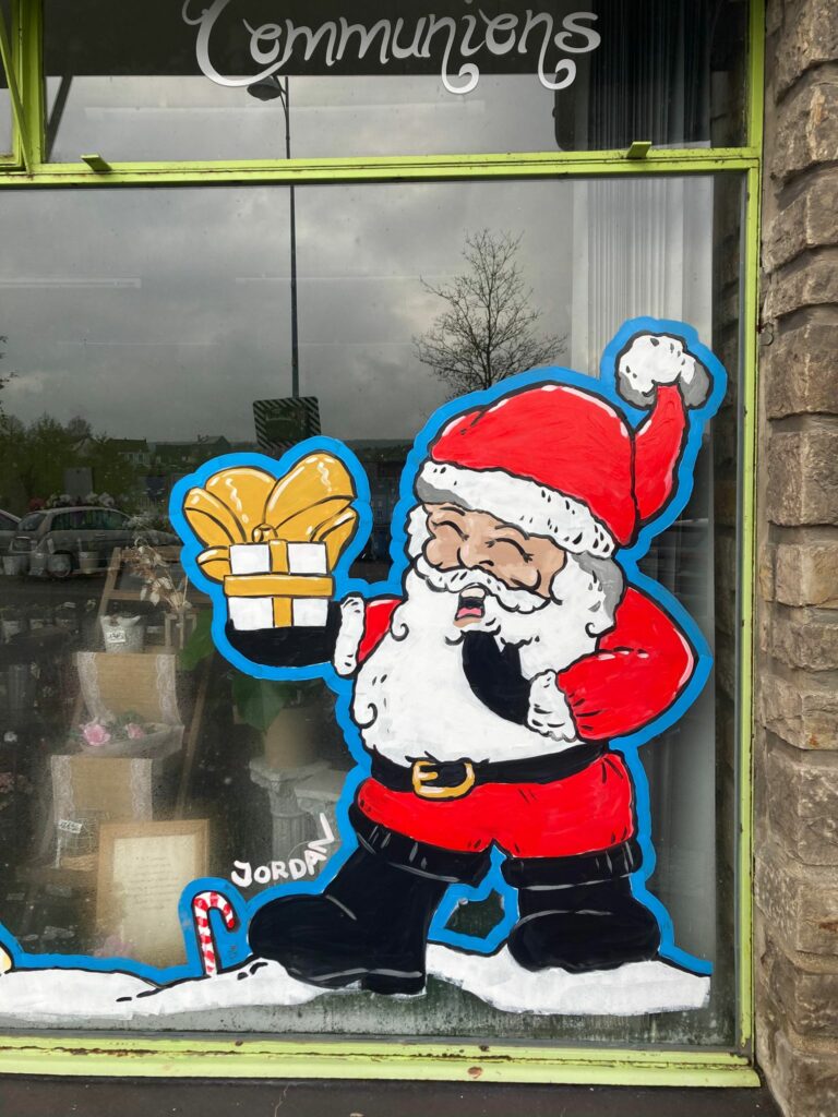 Peinture sur vitrine avec Père Noel en habits rouges offrant un cadeau