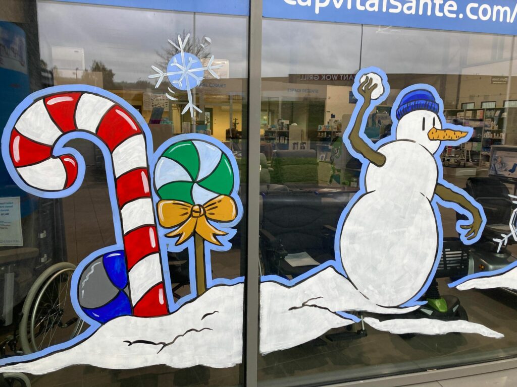 Peinture sur vitrine avec un bonhomme de neige qui lance une boule de neige et des bonbons géants colorés à côté