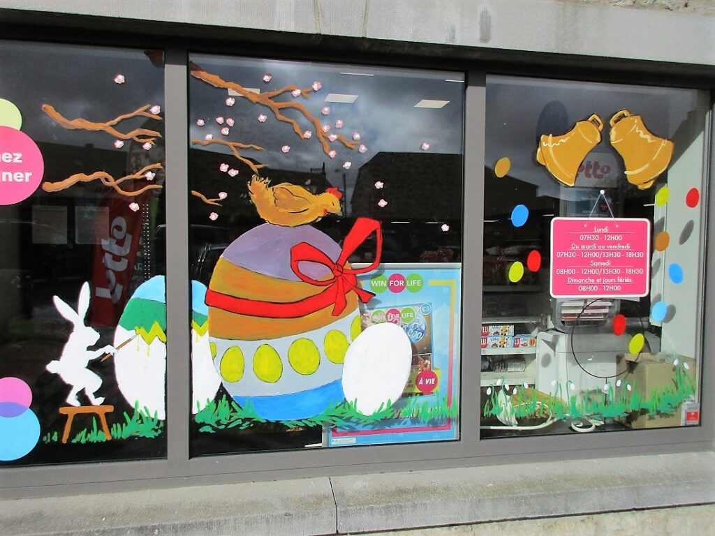 vitrine peinte pour Pâques avec des oeufs colorés, un lapin et un poule. Le tout est peint dans des couleurs vives